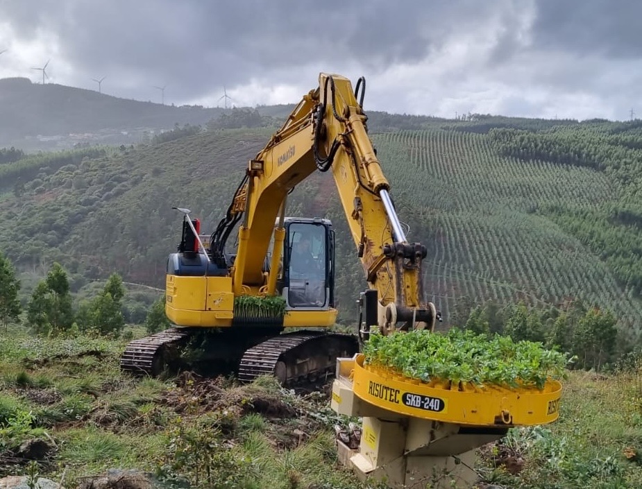 Tracked excavator with a mechanised tree-planting head on a reforestation slope